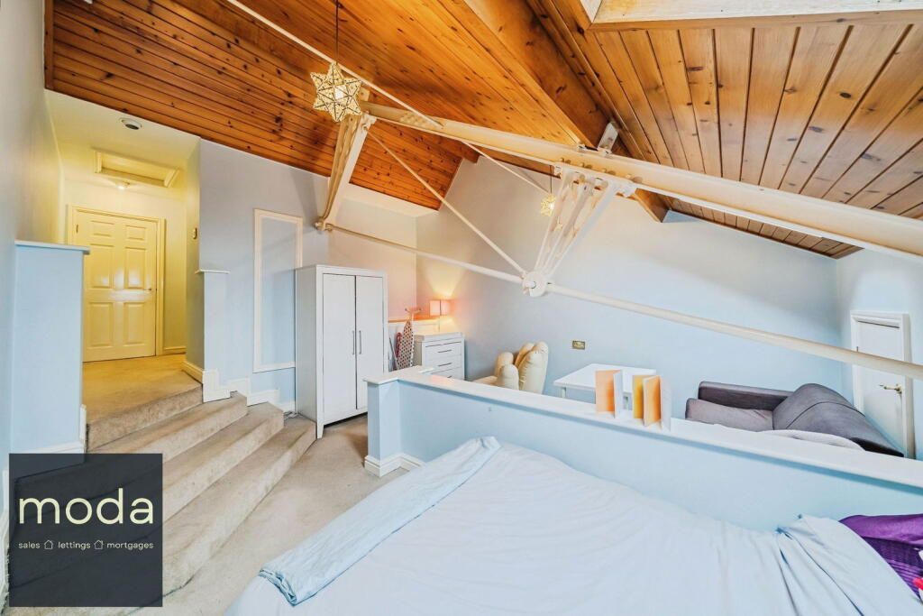 Bedroom with sloped ceiling, exposed wood beams, light blue walls, and a white bed.