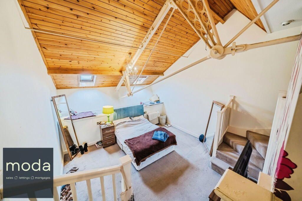 Bedroom with wood ceiling, white walls, bed with brown blanket, and staircase.
