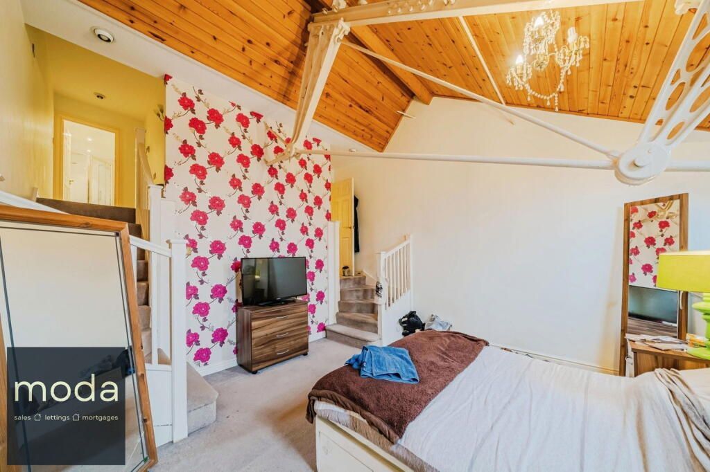 Bedroom with floral wallpaper, wooden beams, bed, TV, stairs, and a chandelier.