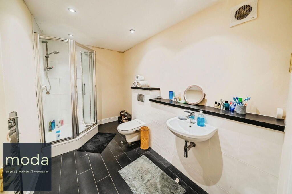Bathroom with shower, toilet, and sink; black tiled floor, beige walls, and white fixtures.