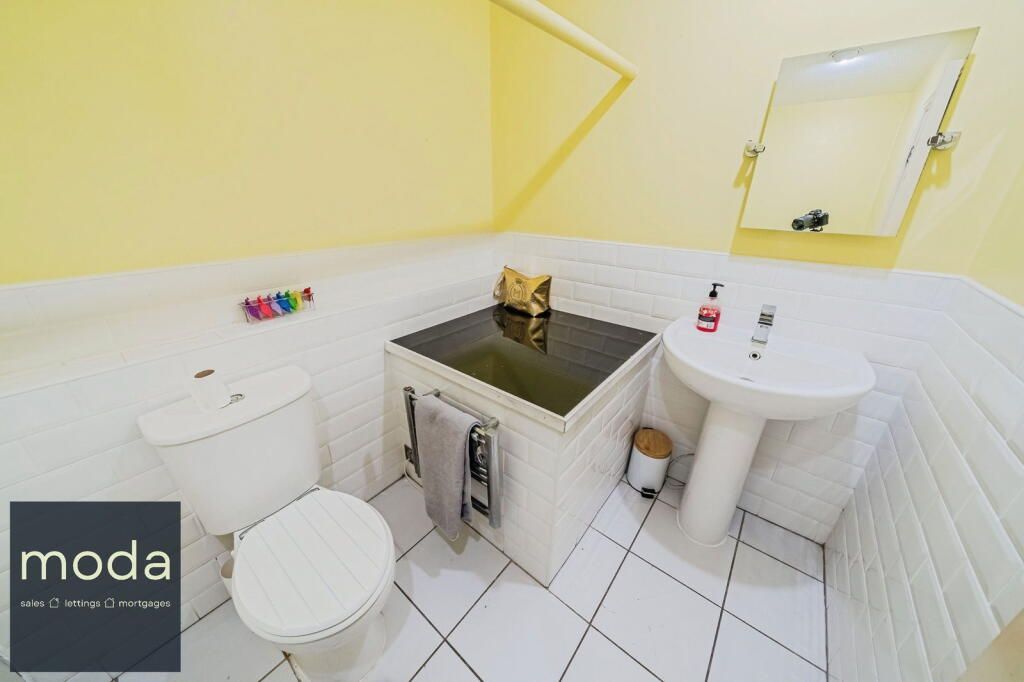 Bright yellow bathroom with toilet, sink, and a small countertop. White tiled floor and walls.