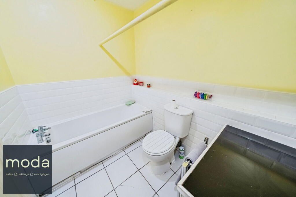 Bathroom with white tiled walls and floor, a white bathtub, toilet, and yellow walls.