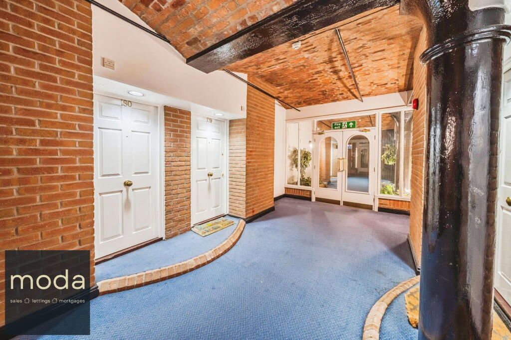 Hallway with blue carpet, exposed brick ceiling, and white doors.
