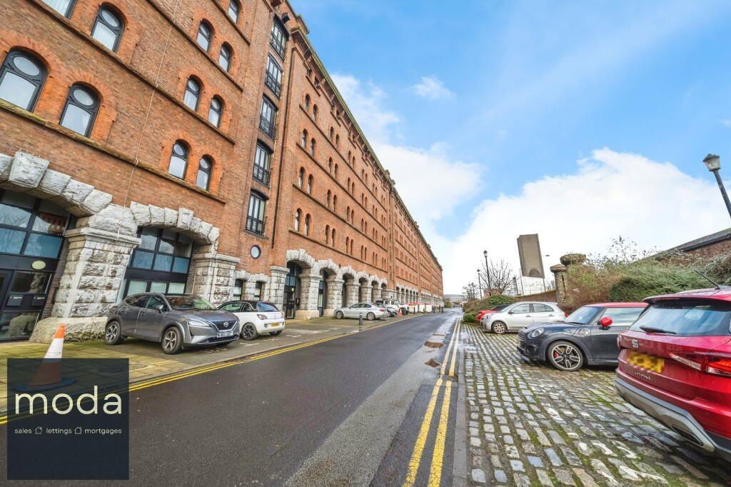 Red brick building with cars parked on cobblestone street, cloudy sky.