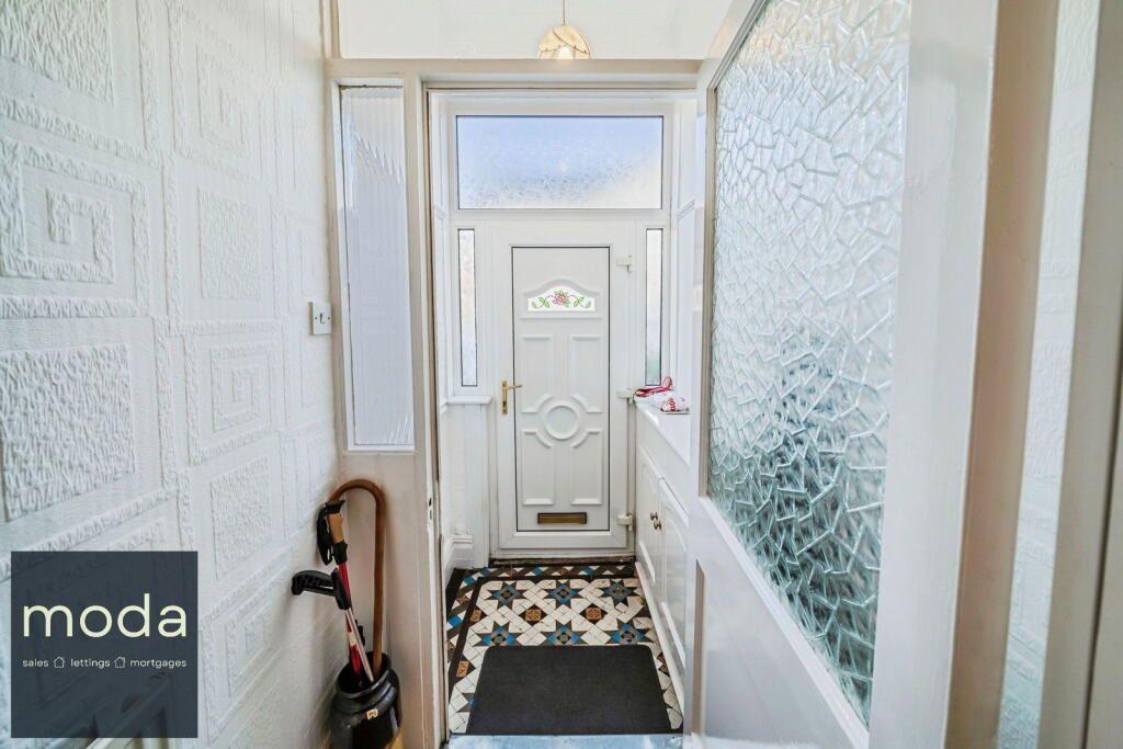 Narrow entryway with patterned tile floor, white walls, front door. Umbrella and bag hang on left.