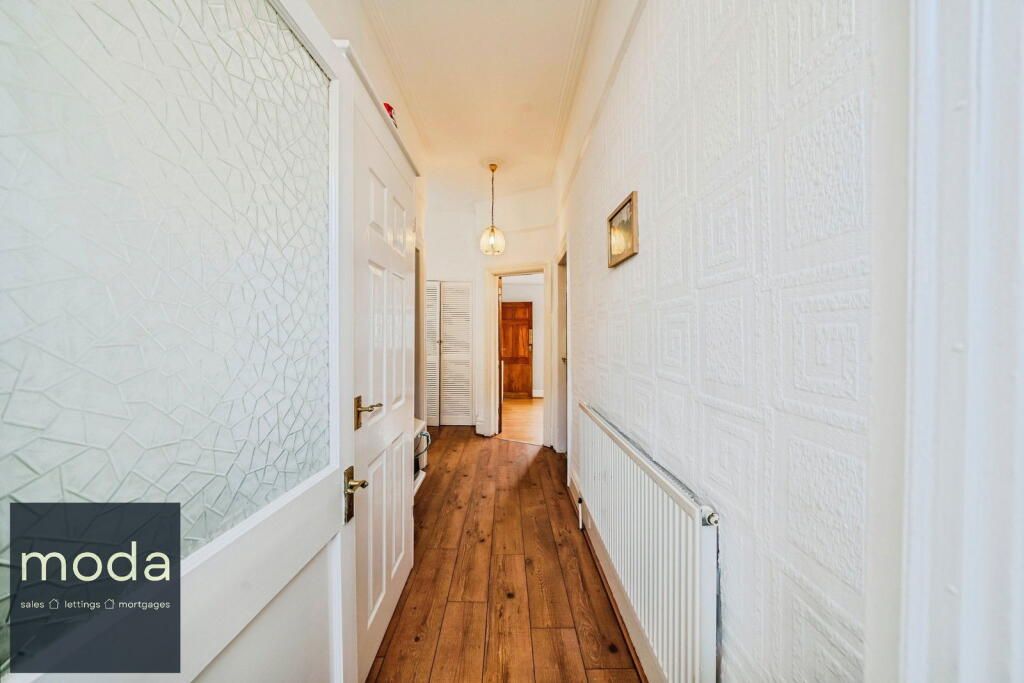 Long hallway with hardwood floors, white walls, radiator, and doors leading to other rooms.