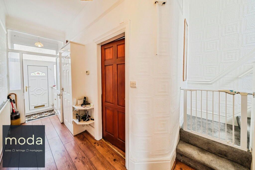 Hallway with wooden floor, white walls, brown door, and staircase with safety gate.