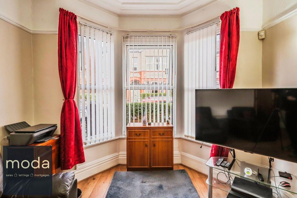 Living room with bay windows, red curtains, vertical blinds, wooden cabinet, and a TV.