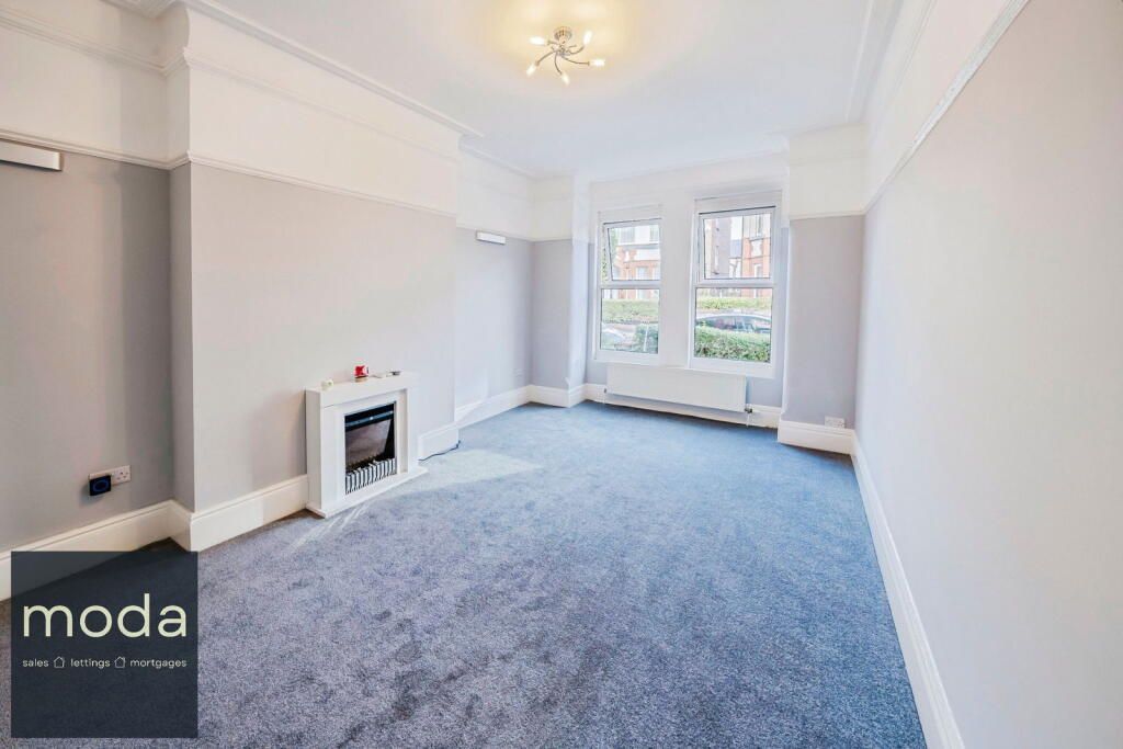 Empty living room with grey walls, blue carpet, fireplace, and windows.