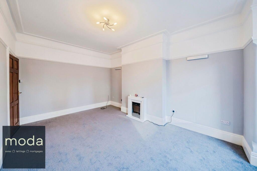 Empty room with light gray walls, blue carpet, white trim, and a fireplace.