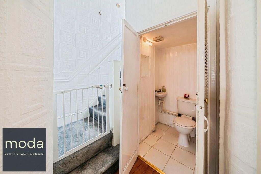 Narrow hallway with stairs, adjacent to a small white bathroom with toilet and sink.