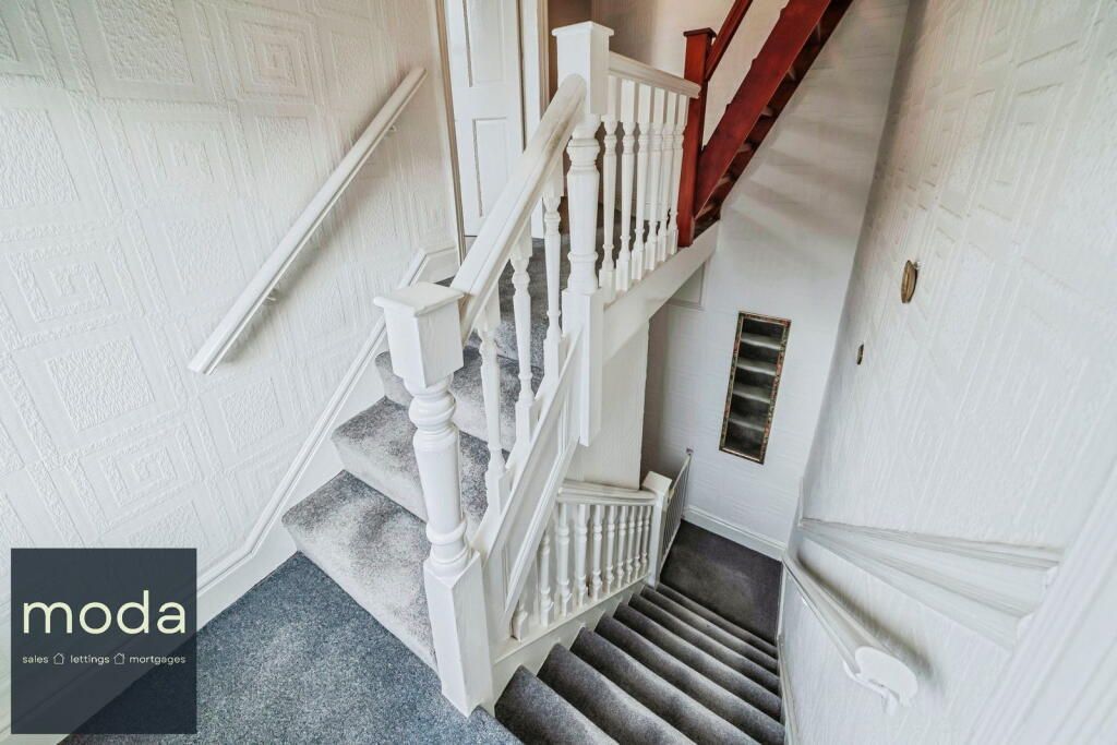 Staircase with white banister, gray carpet, and white walls. Sunlight brightens the space.