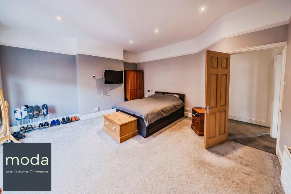Spacious bedroom with a bed, wardrobe, and TV, featuring a wooden door and a chest on a soft carpet.