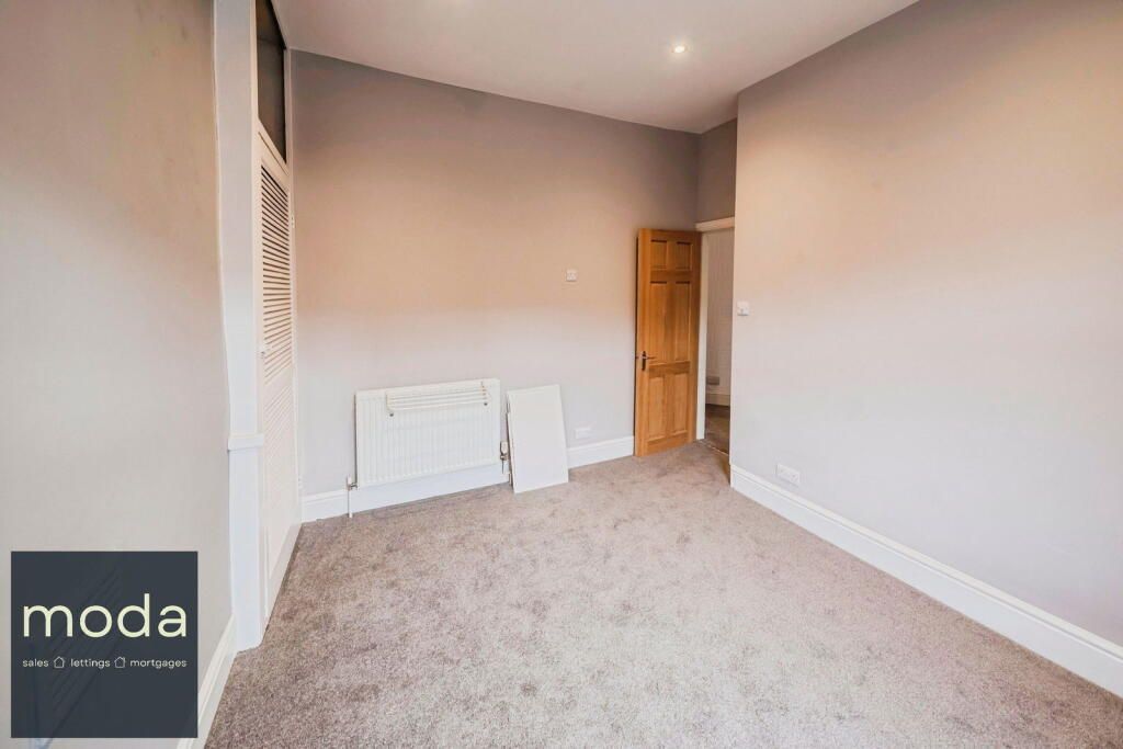 Empty room with gray walls and carpet, a radiator, and a doorway.