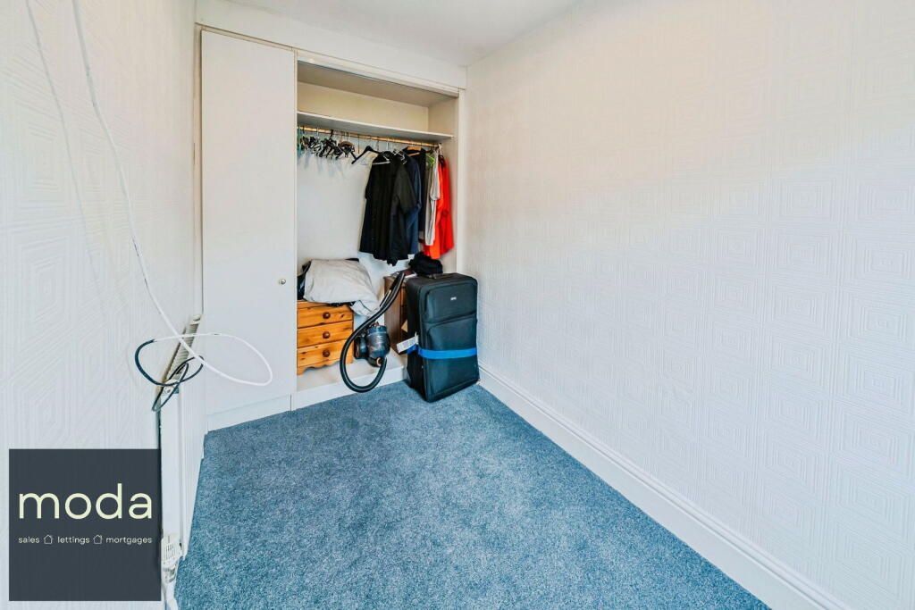 Small room with a closet; blue carpet, white walls. Clothes hang in the closet; a bike and luggage are inside.