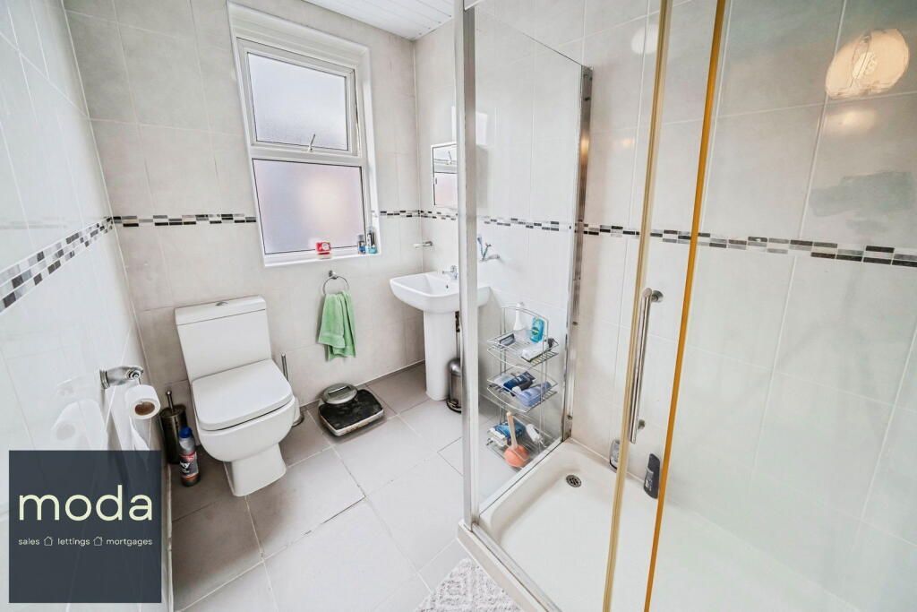 Bathroom with white tiles, toilet, sink, shower stall, and small window.