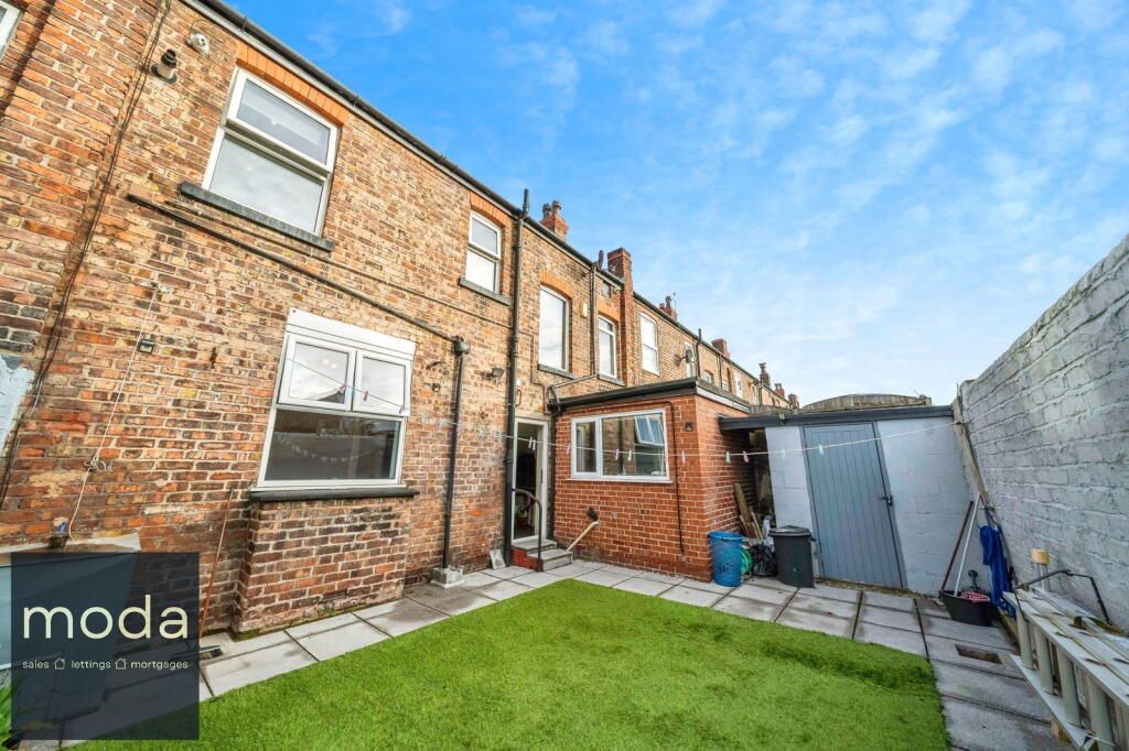 Backyard of brick row houses with small lawn, shed, and stone patio.