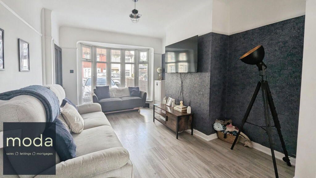 Living room with gray walls, bay window, sofa, TV, lamp, and wooden floor.