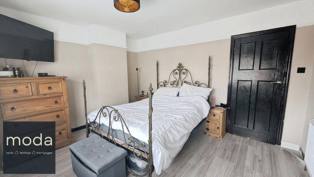 Bedroom with bed, dresser, television, and dark door; neutral colors.