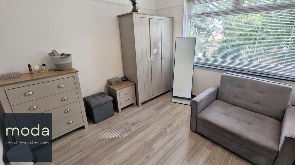 A bedroom with a dresser, wardrobe, chair, mirror, and window. Light wood-look flooring and grey furniture.