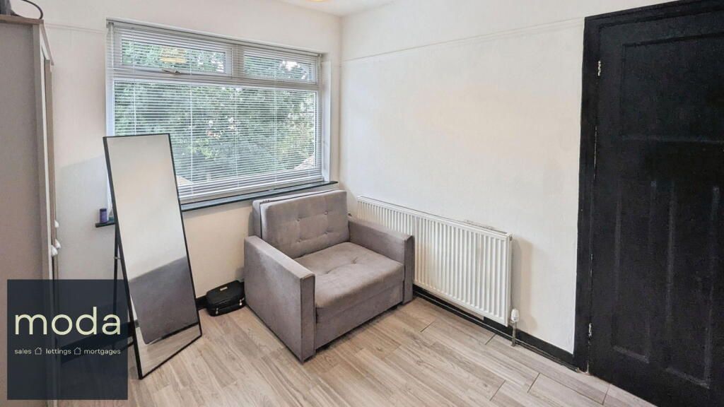 Bedroom with gray armchair, full-length mirror, window, white radiator, and black door.