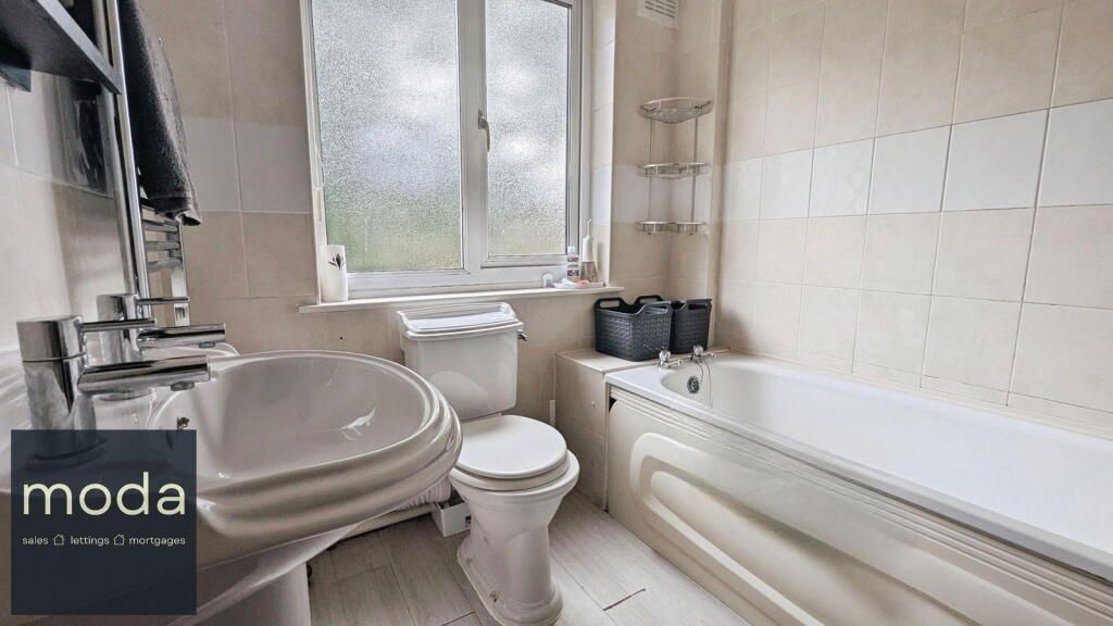 Bathroom with a white sink, toilet, bathtub, and window; cream-colored tile on the walls.