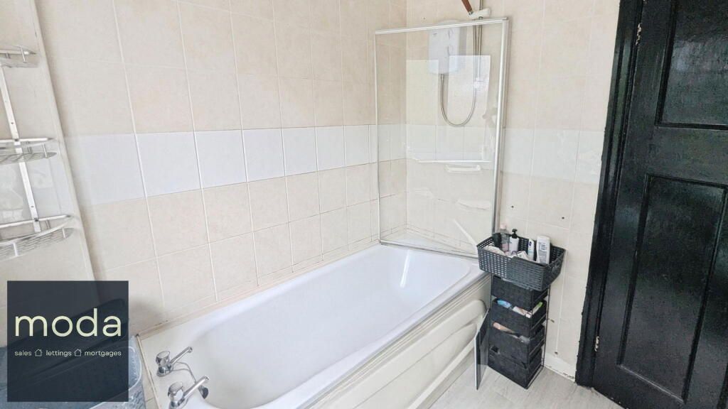 Bathroom with bathtub, shower screen, black door, and cream-colored walls.