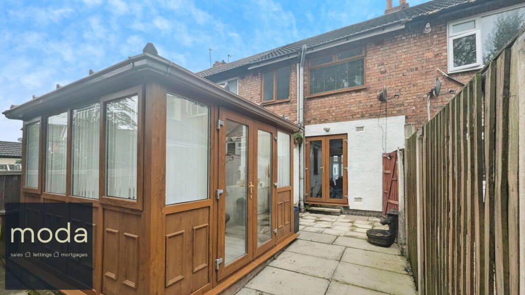 Backyard with sunroom, patio, and house; wooden sunroom and fence on left, brick building on right.