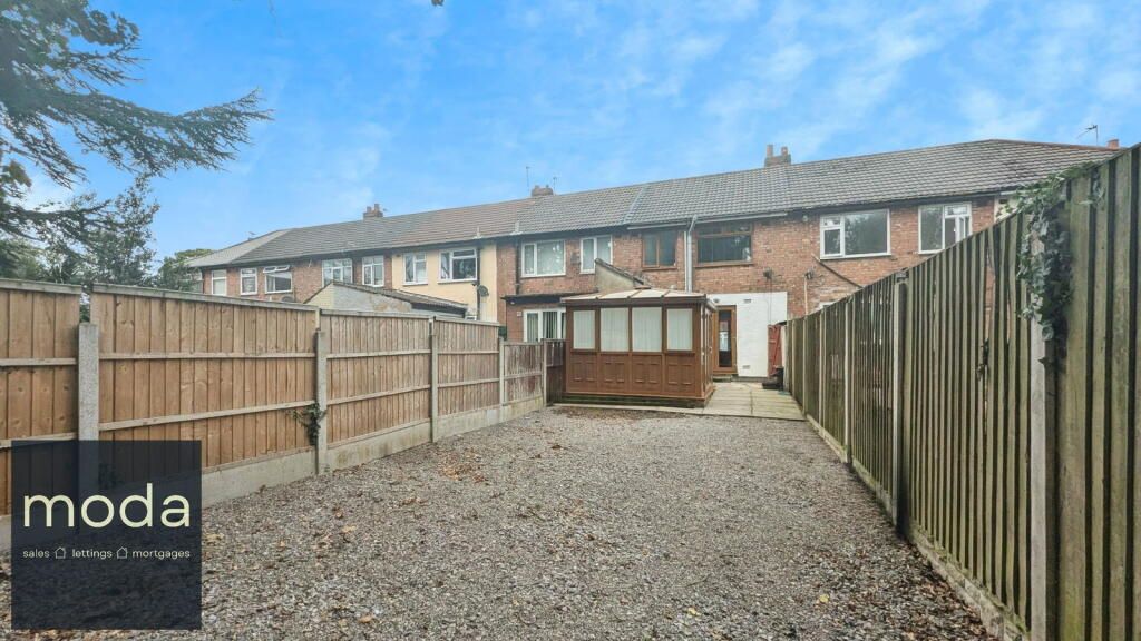 Backyard of a row house with a gravel yard, wooden fences, and a small structure.