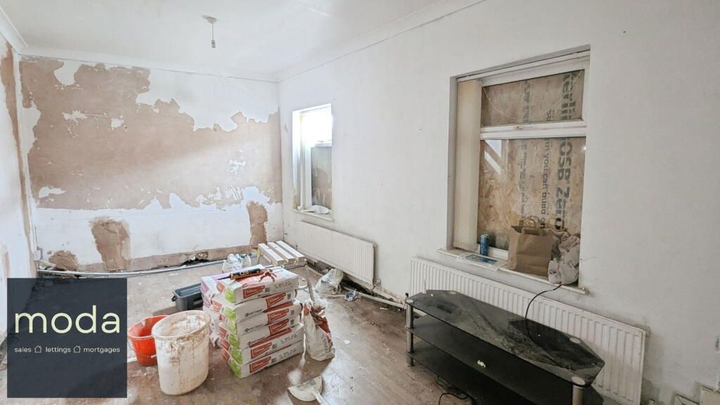 Room under renovation: peeled walls, radiator, window with exposed materials, tools and supplies on the floor.