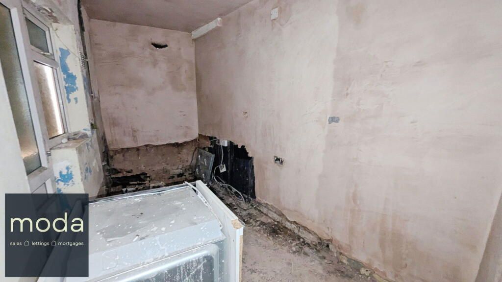 Damaged kitchen with peeling walls, dark mold, and partially exposed appliance.