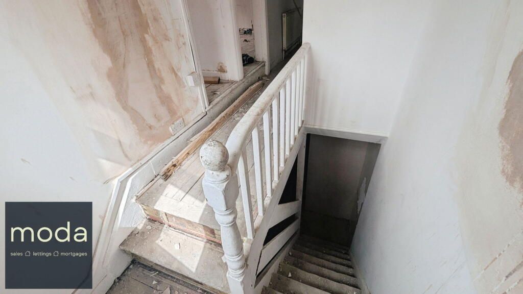 A dilapidated staircase with white banisters and steps. The walls show signs of wear and repair.