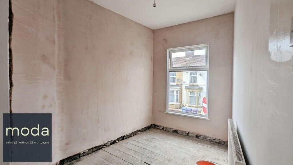A room with exposed walls, window, and unfinished floor. The walls are light pink.