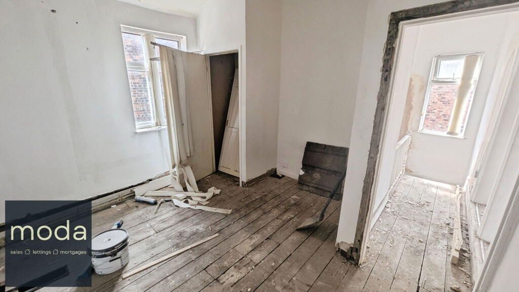 A room in disrepair with exposed wooden floors, a window, and an open doorway.