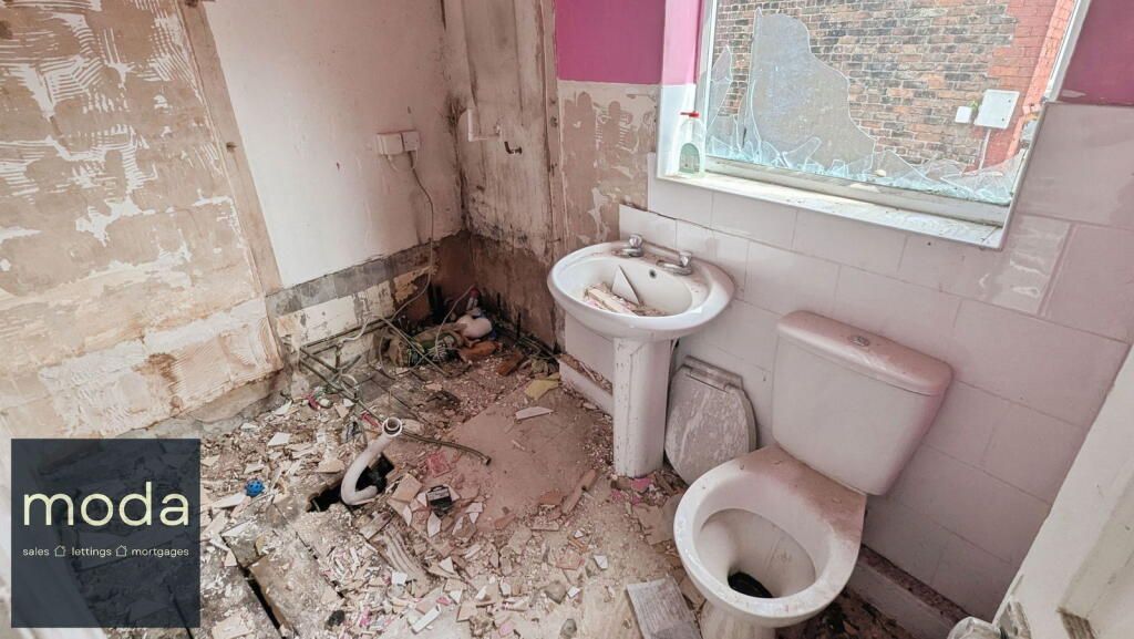 Bathroom under renovation; exposed walls, toilet, sink, debris on floor, window.
