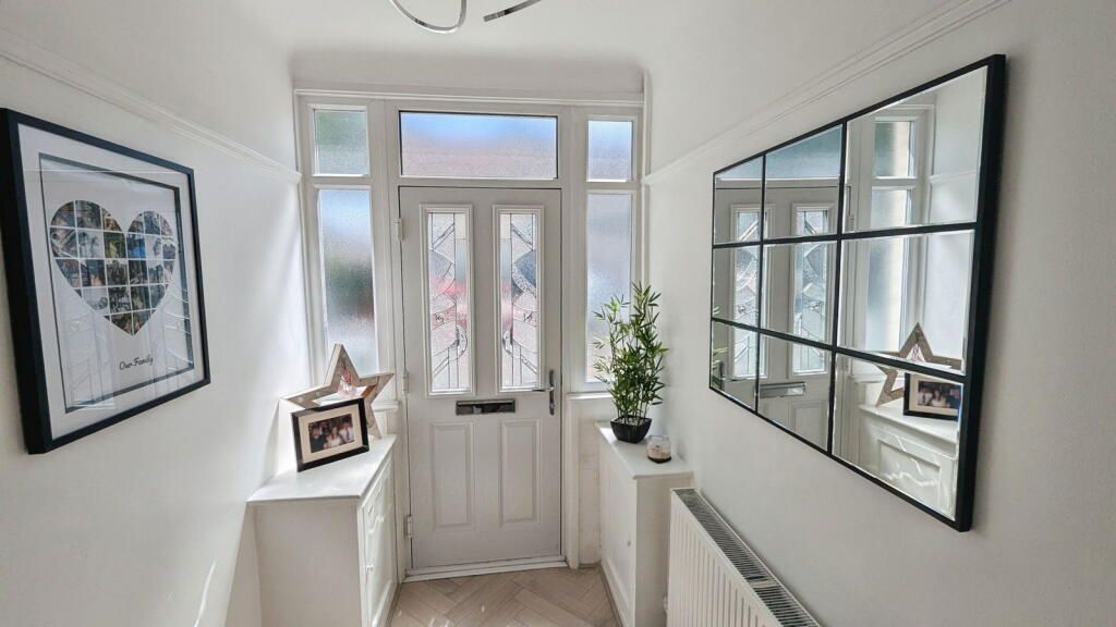 Narrow white hallway with a front door, framed mirror, and a picture.