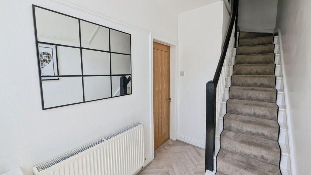 Hallway with stairs on the right, mirror and radiator on the left, wooden door in the center.