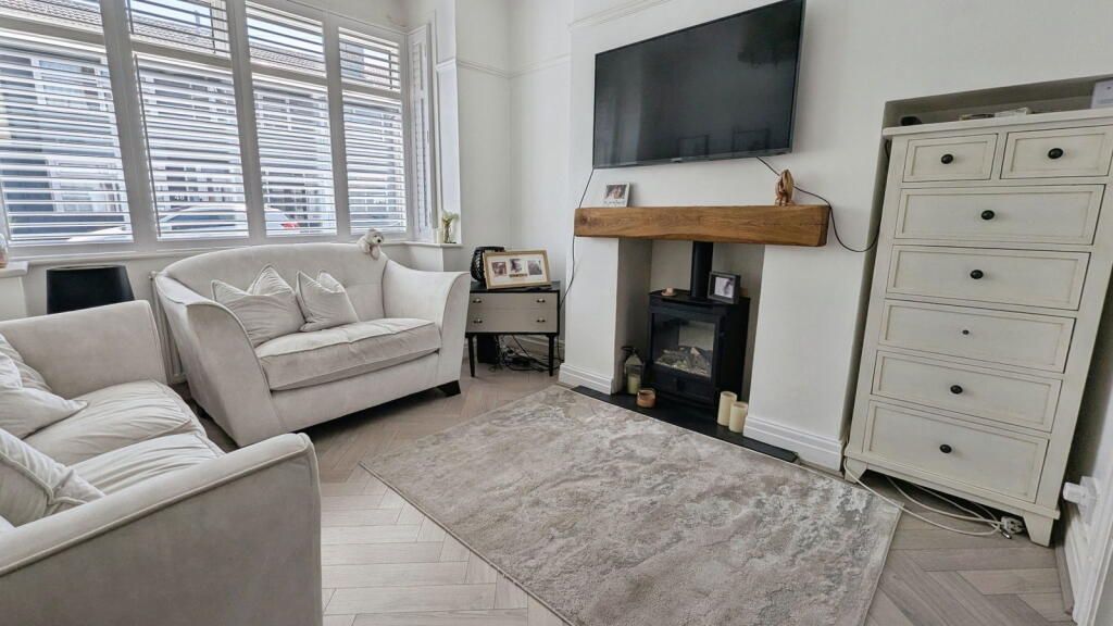 Living room with white furniture, fireplace, and rug. Light-filled with a window and wooden floor.