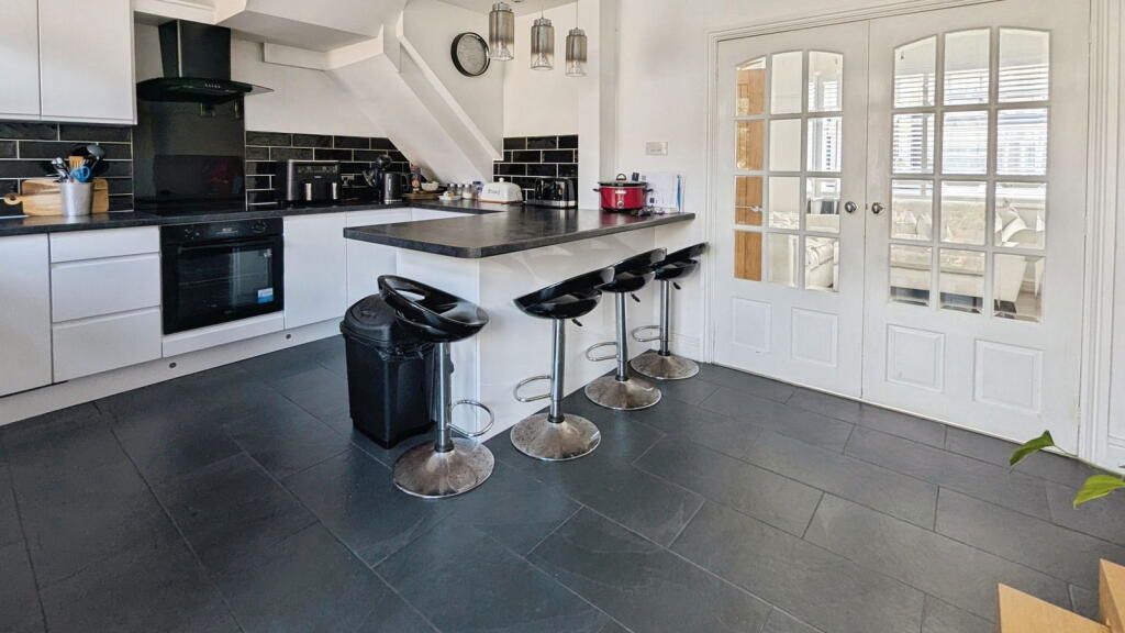 Modern kitchen with white cabinets, black countertops, and bar stools. French doors lead outside.