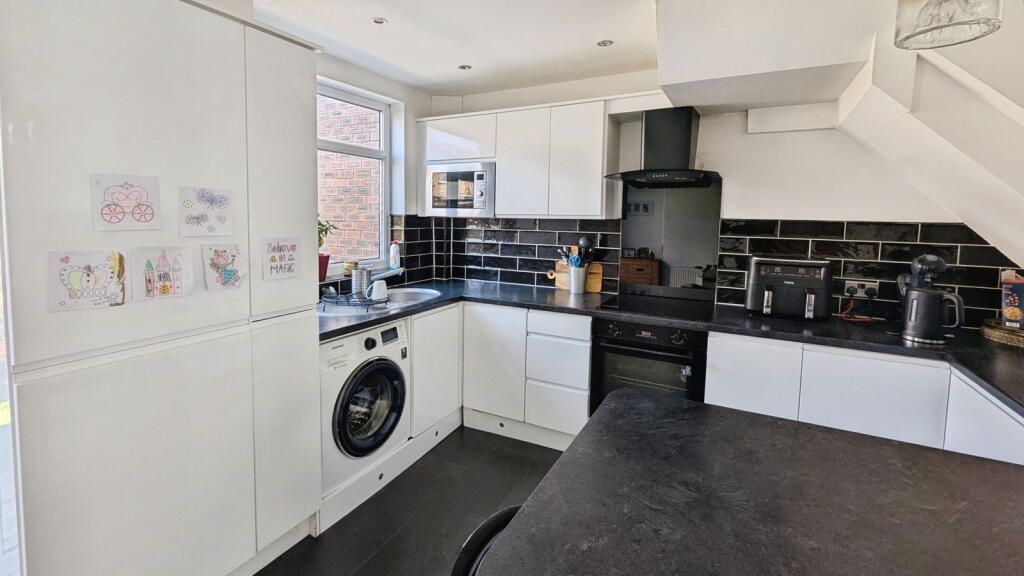 Modern white kitchen with black countertops and accents, featuring appliances and artwork.