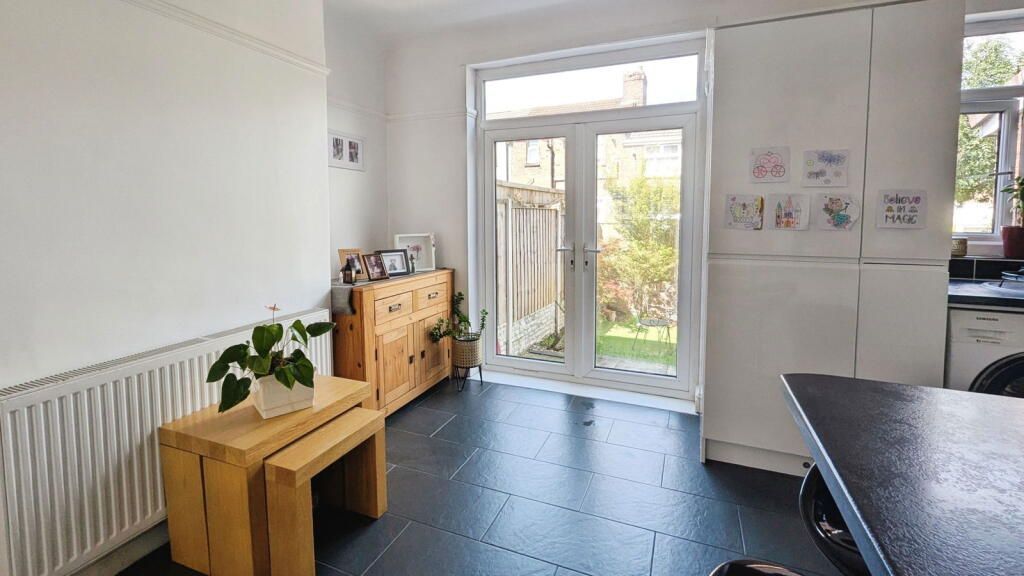 Bright kitchen with black floor, wooden table and cabinet, leading to a garden door.