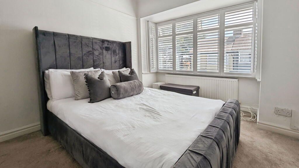 Bedroom with gray velvet bed, white bedding, and window with shutters.