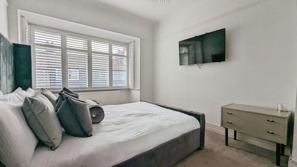 Bedroom with bed, window with blinds, TV, and a nightstand.