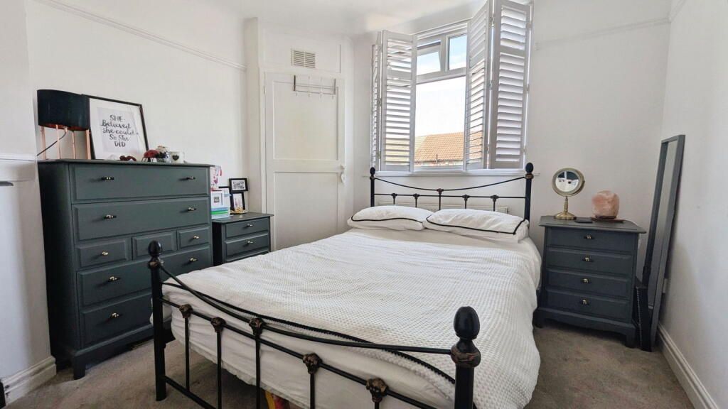 Bedroom with bed, dresser, nightstands, window with shutters; white walls, dark furniture.