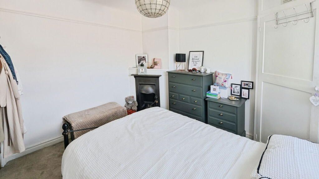 Bedroom with white walls, bed, green dressers, fireplace, and a decorative light fixture.