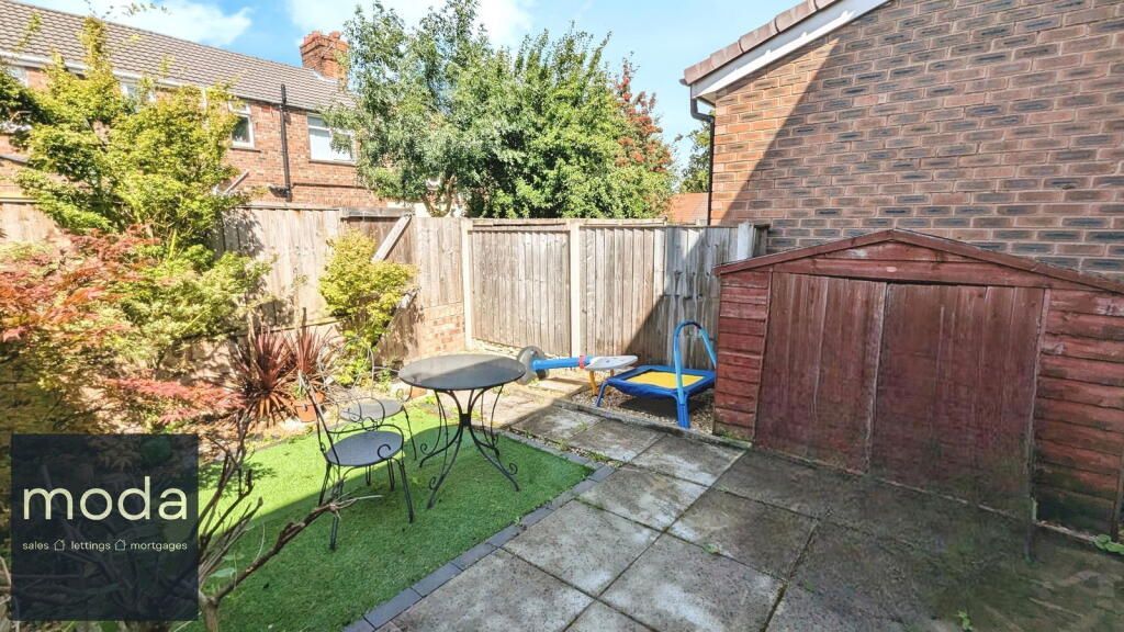 Small backyard with patio, green turf, table, chairs, and shed. Wooden fence in background.