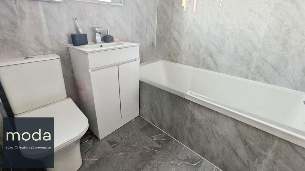 Bathroom with white toilet, sink cabinet, bathtub. Gray stone-look tile.
