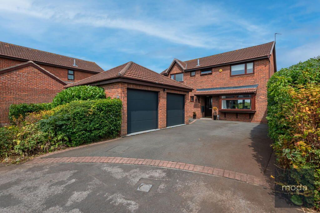 Two-story brick house with attached garage and driveway, under a blue sky.