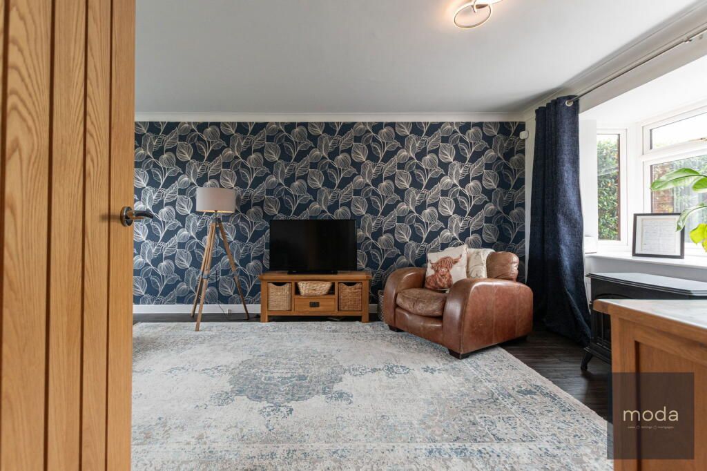 Living room with patterned wallpaper, leather armchair, rug, and wood furniture.