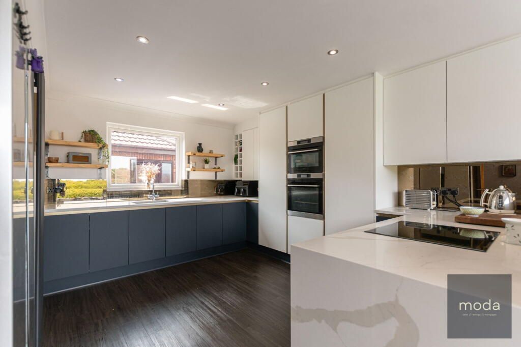 Modern kitchen with white cabinets, dark blue lowers, dark wood floors, and stainless steel appliances.